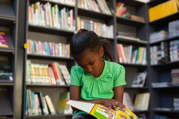 学校の図書館で本を読んで集中かわいいアフリカ系アメリカ人女学生の正面図 — ストック写真