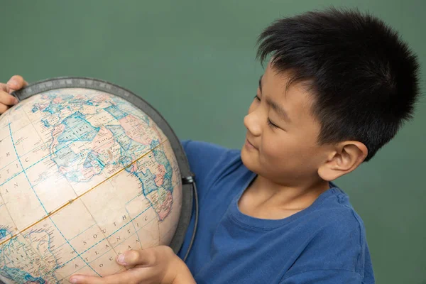 小学生在小学教室里站在绿色黑板上看着地球仪的正面 — 图库照片