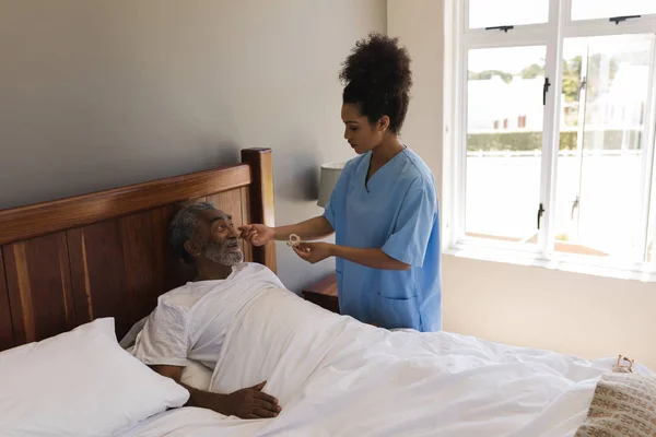 在一名年轻的非洲裔美国女医生在家中的卧室里给一名非洲裔美国高级男子安装助听器的正面看法 — 图库照片