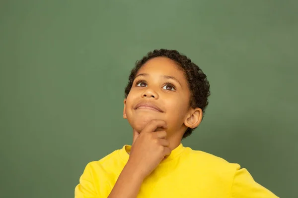 小学校の教室で緑色の基板に対して立っている思慮深い混血少年の正面図 — ストック写真
