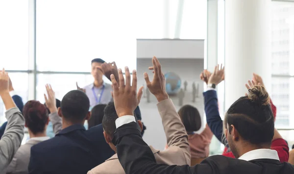 アジア系のビジネスマンが事務所ビルでのビジネス セミナーで話している間に 手を上げるさまざまなビジネス人々 の背面図 — ストック写真