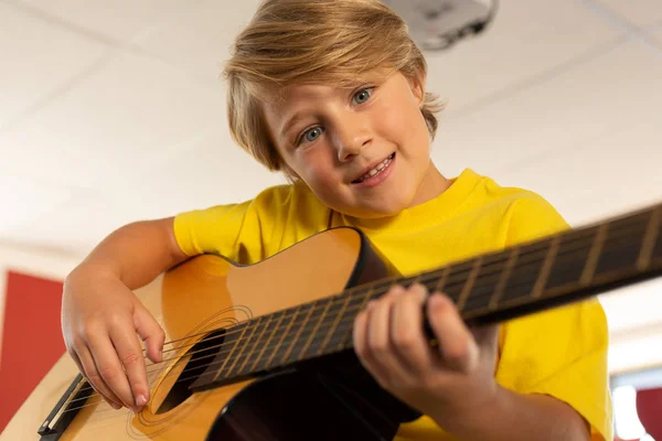 白人少年の小学校で教室でギターを弾きながらカメラ目線の正面図 — ストック写真