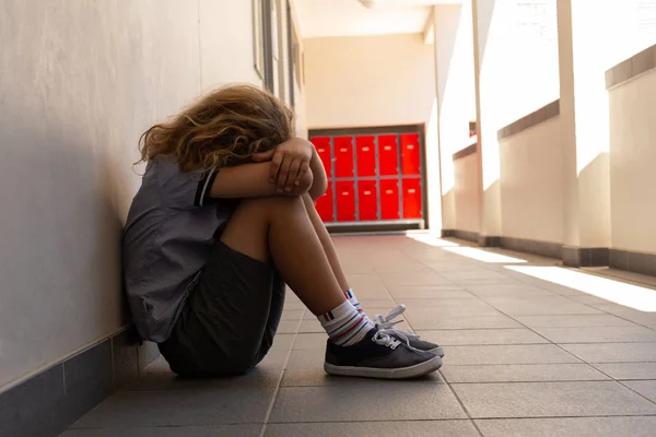 在学校走廊里 悲伤的小学生低着头坐在地板上的侧视图 — 图库照片