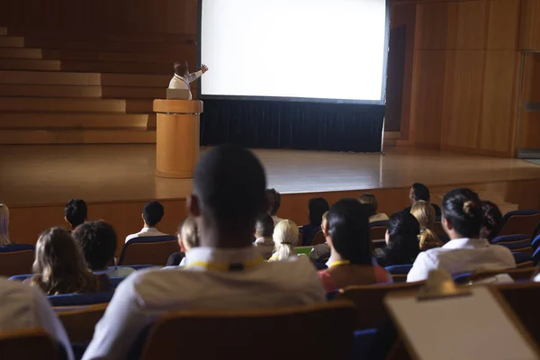 Front view of old African-American businessman standing around podium and giving presentation in the auditorium