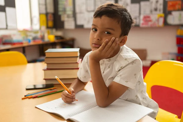 在小学的一间教室里 有思想的混血小学生在桌子上用一只手在桌子上学习 — 图库照片