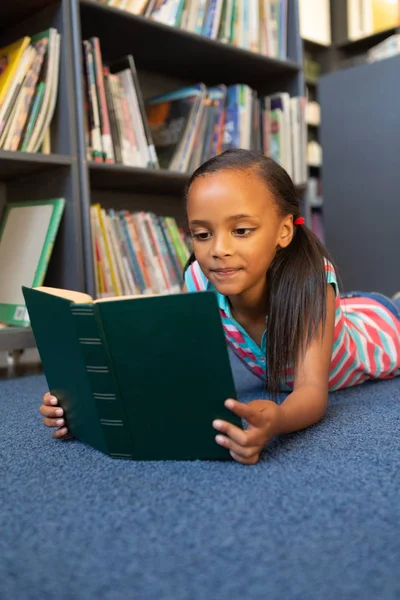 学校の図書館で本を読んで混血女子高生の正面図 — ストック写真