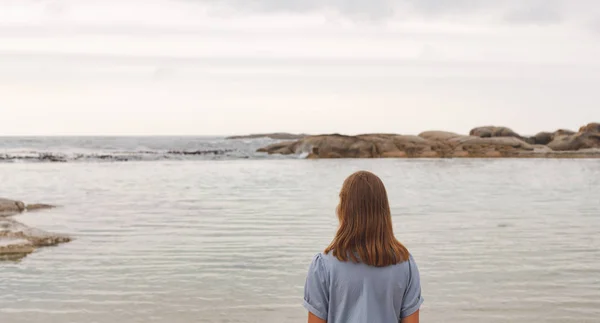 ビーチに立っている若い白人女性の背面 彼女は海を見ています — ストック写真