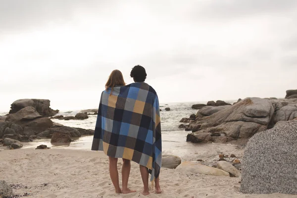 Vista Trasera Joven Pareja Caucásica Envuelta Manta Pie Playa Están —  Fotos de Stock