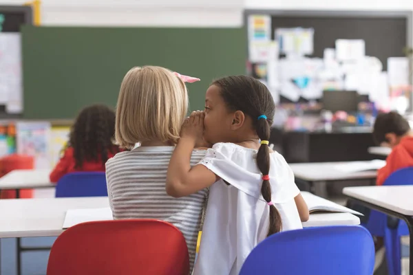 Rear View Schoolgirl Whispering Her Friend Ear Classroom School — Stock Photo, Image