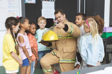 Front view of firefighter teaching student about fire safety while holding fire helmet clipart