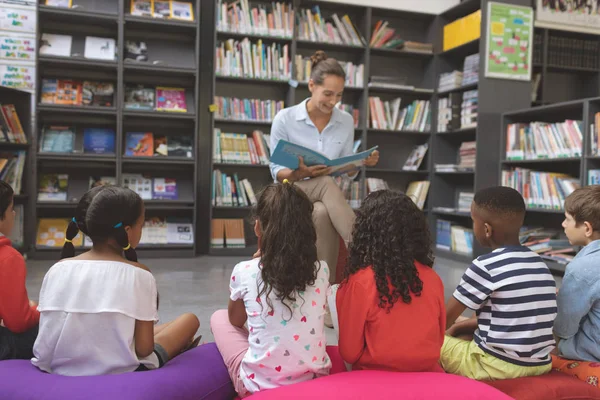 先生の正面図子供たちに図書館で物語を読んで 前景にある大きな色のクッションの上に座っている — ストック写真