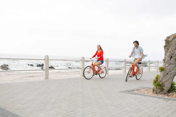 在海滩长廊附近的人行道上骑自行车的年轻高加索夫妇的侧视图 — 图库照片
