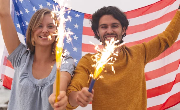 年轻的高加索夫妇的肖像玩火饼干 而举行美国国旗 他们面带微笑 看着镜头 — 图库照片