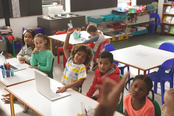 在学校里 一排排的孩子听老师讲课 其中一个孩子举起手指在学校的课堂上回答一个问题 — 图库照片