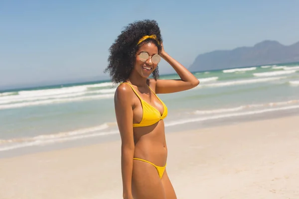 穿着黄色比基尼和太阳镜的快乐的非洲裔美国妇女的肖像站在海滩上 她面带微笑 看着照相机 — 图库照片