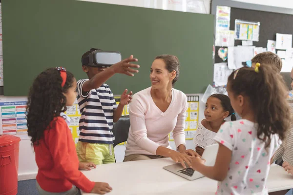 彼の隣に彼のクラスメートと彼女の先生と教室で学校でバーチャルリアリティヘッドセットを使用して男子生徒の正面図 — ストック写真