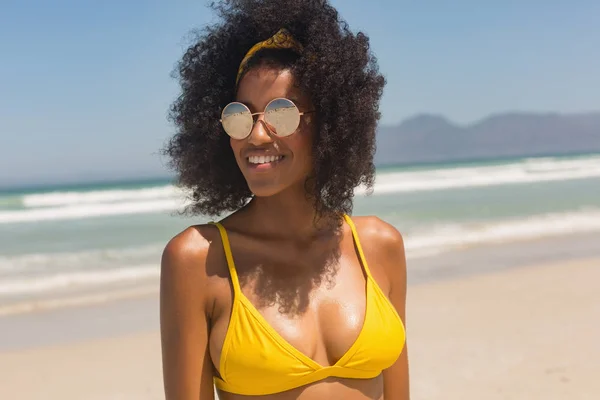 黄色ビキニでビーチに立ってサングラス幸せの若いアフリカ系アメリカ人女性の背面 彼女は笑っています — ストック写真