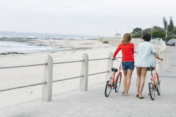 在海滩长廊附近的人行道上散步时 高加索青年夫妇拿着自行车走在后面的景色 — 图库照片