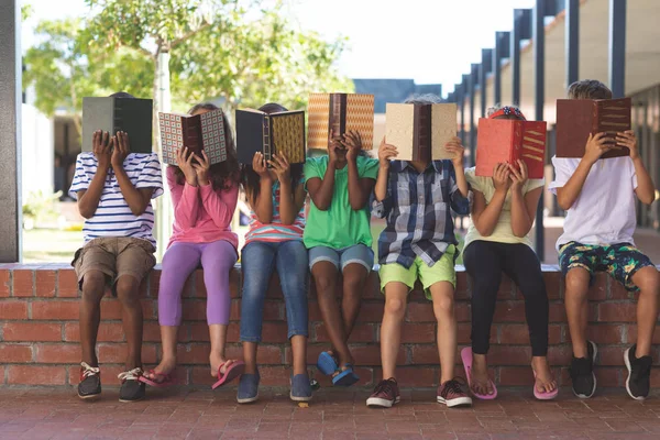Okul Koridorunda Tuğla Duvarda Otururken Kitapların Arkasına Saklanan Çok Etnik — Stok fotoğraf