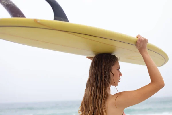 ビーチで彼女の頭の上にサーフボードを運ぶ若い女性サーファーの後姿 彼女が離れています — ストック写真