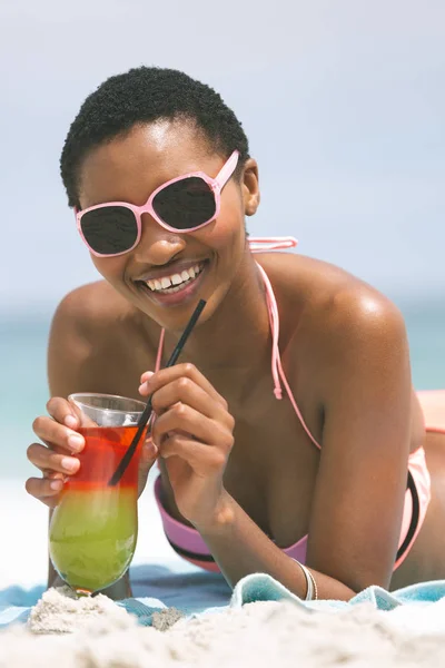 在阳光明媚的日子里 非洲裔美国妇女躺在海滩上喝鸡尾酒汁的正面景色 — 图库照片