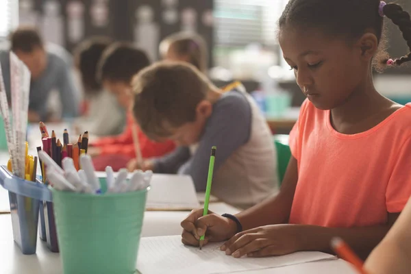 Zbliżenie Mixed Race Girl Szkoły Pisania Swoim Notebooku Klasie Przeciwko — Zdjęcie stockowe