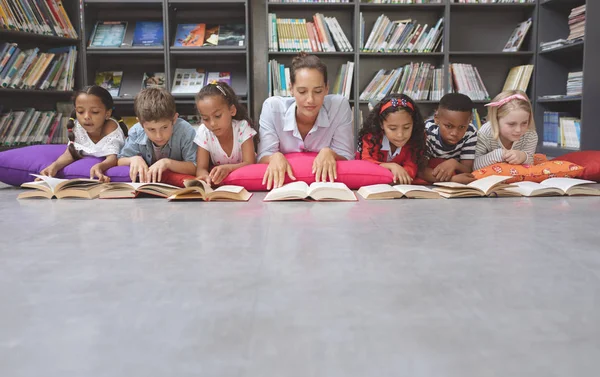 学校で図書館で彼の学校の子供たちと一緒にクッションや読書のために横たわっている教師の正面図 — ストック写真