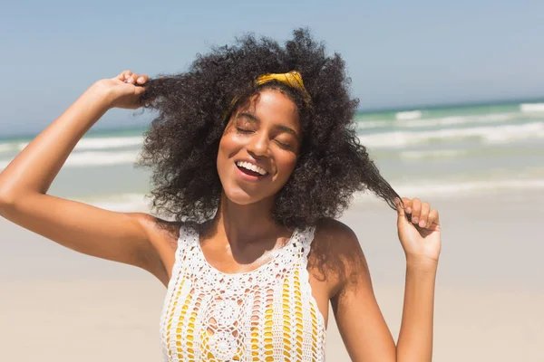 前面的看法 快乐的年轻非洲裔美国妇女闭着眼睛玩头发站在海滩上 她在微笑 — 图库照片