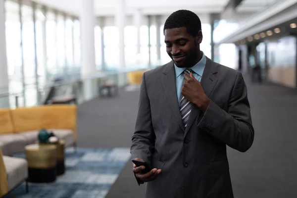 近代的なオフィスに立って携帯電話を使用して 若いアフリカ系アメリカ人のビジネスマンの正面図 笑っている — ストック写真
