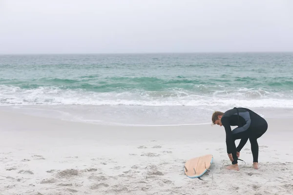ビーチで彼の足にサーフボード リーシュを結ぶ若い白人男性サーファーの背面図 — ストック写真