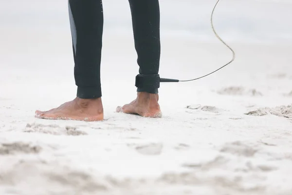 ビーチで彼の足に彼のサーフボード リーシュと立っている若い男性サーファーの低いセクション — ストック写真