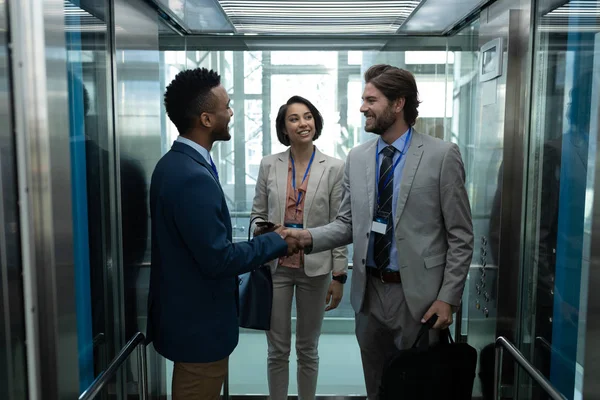 立っていると握手 エレベーターの中で お互い相互作用ビジネス部門の同僚の若い多民族ビジネス同僚の正面図 — ストック写真
