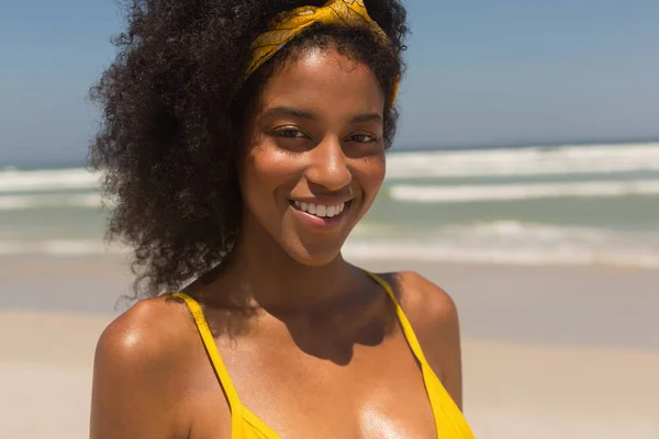 黄色いビキニを着てカメラで浜に立って見て幸せな若いアフリカ系アメリカ人女性の肖像画 彼女は笑っています — ストック写真