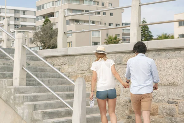 在阳光明媚的日子里 在海滨长廊上 白种人年轻夫妇手牵手走在海边的后景 — 图库照片