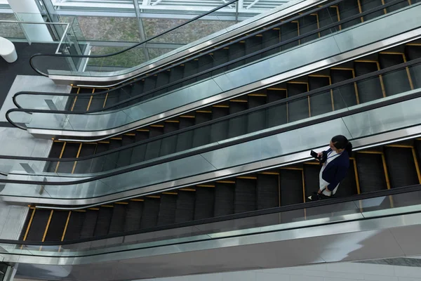 Blandad Ras Affärskvinna Med Mobiltelefon Medan Flyttar Rulltrappa Office Lobby — Stockfoto