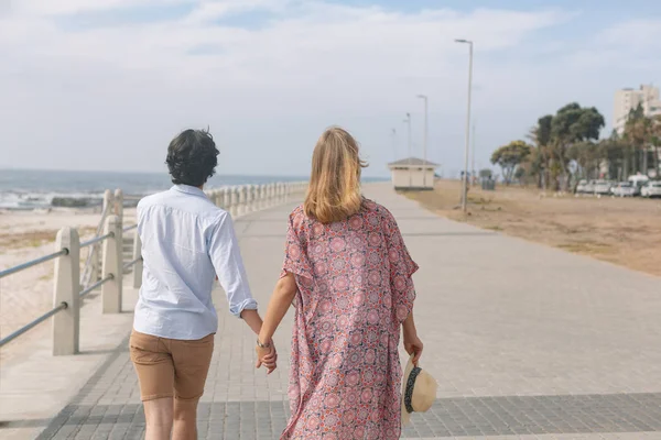 在一个阳光明媚的日子里 在海边的长廊上 年轻的高加索夫妇手拉手走在桥上的后景 — 图库照片