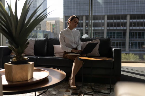 近代的なオフィスのソファに座りながらのラップトップに取り組んでかなり若い白人実業家のフロント ビュー — ストック写真
