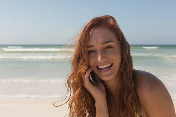 穿着比基尼的快乐美丽的年轻白人妇女在海滩上用手机交谈的肖像 她面带微笑 看着照相机 — 图库照片