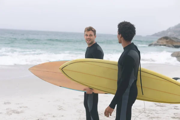 年轻的多民族男性朋友在海滩上互动 同时拿着冲浪板的正面看法 他们在微笑 — 图库照片