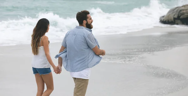 手拉手走在海滩上的情侣的后景 — 图库照片