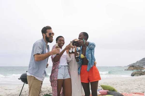 多民族朋友在海滩上喝啤酒时在手机上恢复照片的正面看法 — 图库照片