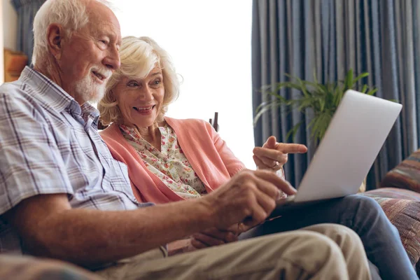 在养老院使用笔记本电脑时 高加索夫妇相互互动的侧视图 一对夫妇坐在沙发上 同时用手指指着笔记本电脑的屏幕 — 图库照片