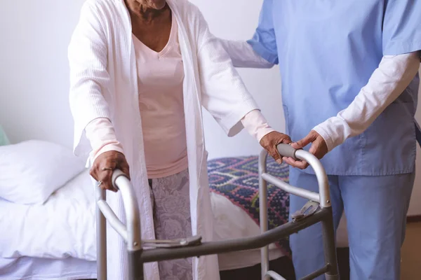 女护士中段帮助老年女性患者与沃克站在一起 — 图库照片