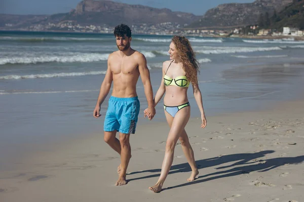 Front view of Caucasian couple walking with hand in hand at beach on a sunny day. They seem happy