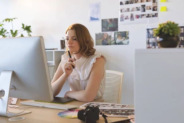 若い白人女性グラフィックデザイナーがオフィスのデスクでグラフィックタブレットとコンピュータで作業していることの正面図 — ストック写真
