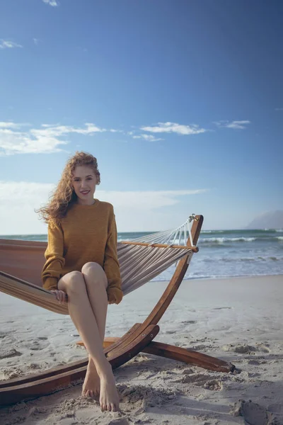 年轻美丽的高加索妇女坐在吊床上的肖像 腿交叉在海滩上 在一个阳光明媚的日子 她面带微笑 看着照相机 — 图库照片
