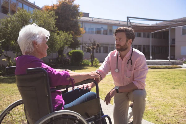 一位白人男医生在退休后的退休经历下与坐在轮椅上的残疾老年病人妇女交谈的侧视图 — 图库照片