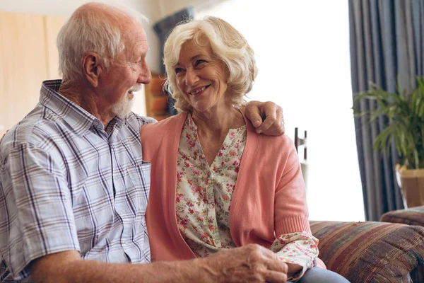 老人ホームでソファに座ってロマンチックな年上の白人のカップルの正面図 二人はお互いに微笑んで抱き合っている — ストック写真