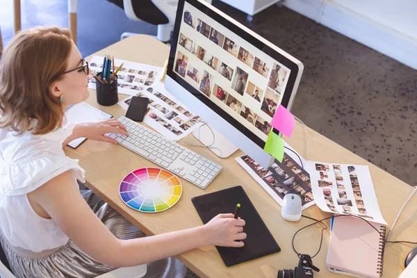 在办公室办公桌上使用图形平板电脑和计算机的年轻高加索女性平面设计师的高角度视角 — 图库照片