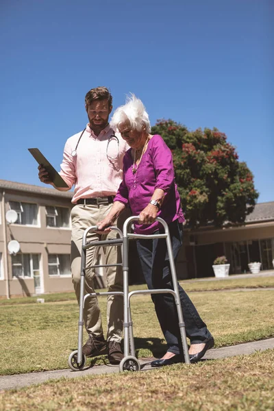 一个自信的高加索医生帮助高级高加索妇女与她的步行者在后院养老院的侧视图 — 图库照片